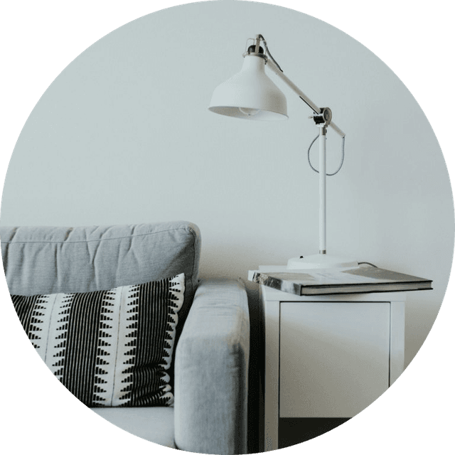 Salon minimaliste avec canapé gris, table d’appoint blanche et lampe.