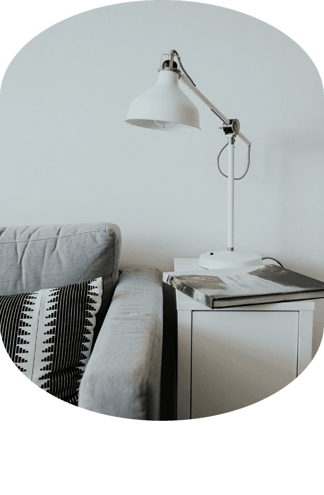 Salon minimaliste avec canapé gris, table d’appoint blanche et lampe.